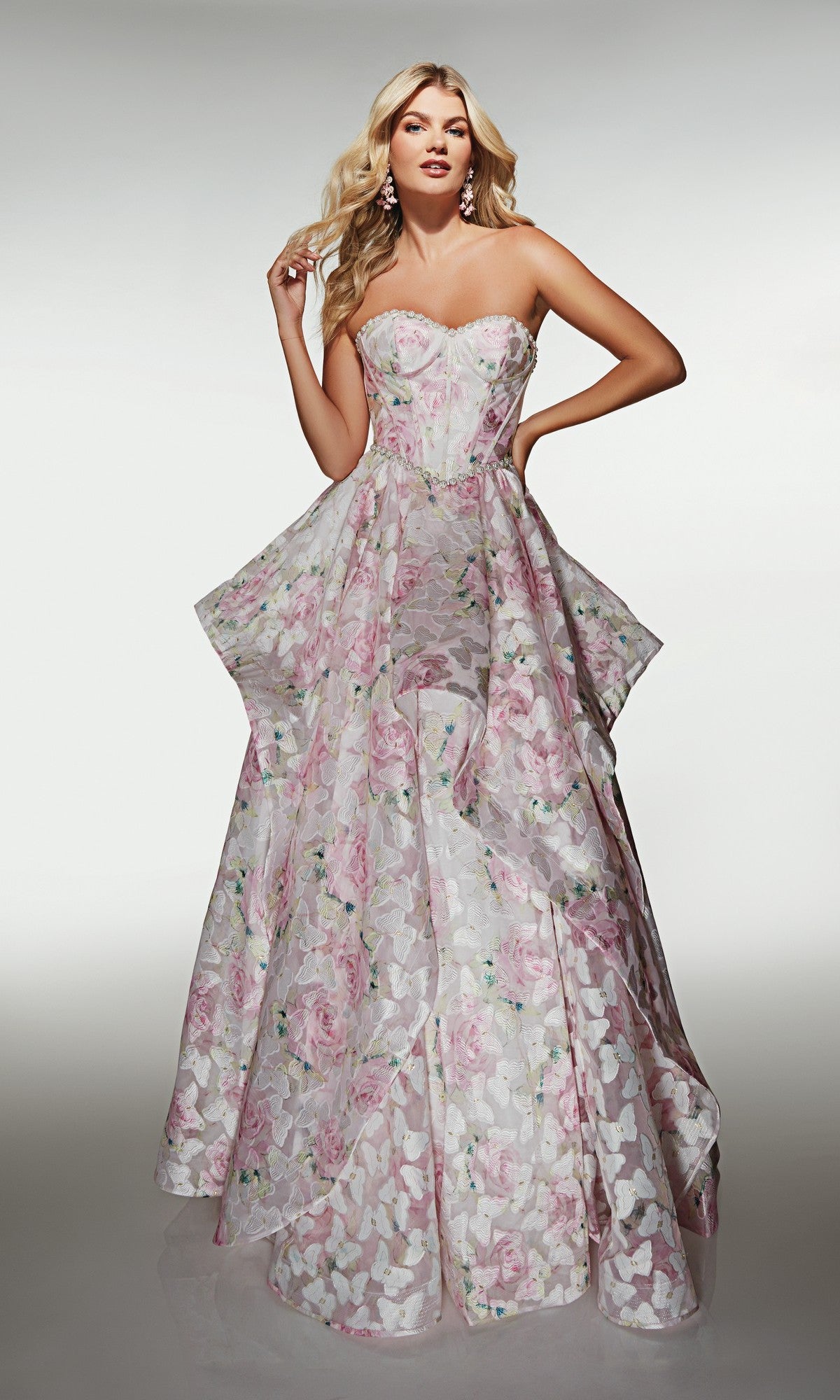 A woman stands against a plain background wearing the Alyce 62071 long prom dress in pink/white, featuring a strapless organza bodice with a pastel floral pattern and a flowing, floor-length skirt.